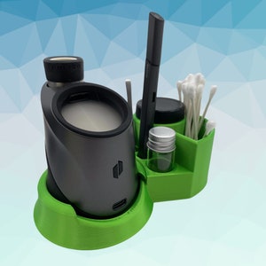K&ouml;nnte beinhalten: Ein gr&uuml;ner und grauer Desktop-Organizer f&uuml;r einen Vaporizer. Der Organizer hat ein Fach f&uuml;r den Vaporizer, ein kleines Glas und ein Fach f&uuml;r Wattest&auml;bchen.