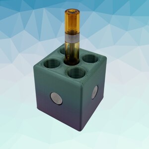 Puede incluir: Un organizador de almacenamiento en forma de cubo verde y morado con seis agujeros redondos para guardar cartuchos de vape. Un cartucho est&aacute; en el organizador.