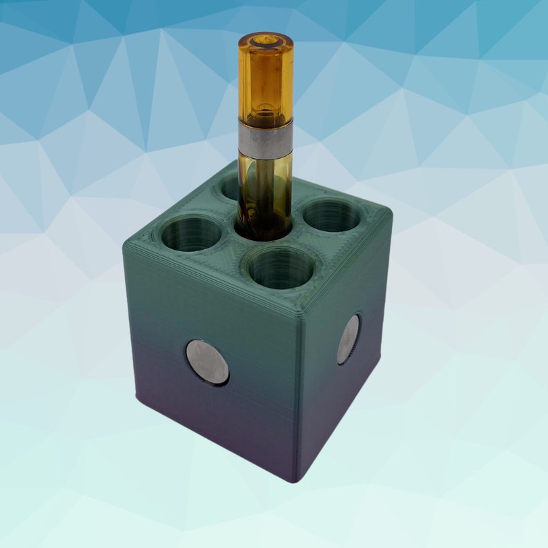 Puede incluir: Un organizador de almacenamiento en forma de cubo verde y morado con seis agujeros redondos para guardar cartuchos de vape. Un cartucho est&aacute; en el organizador.