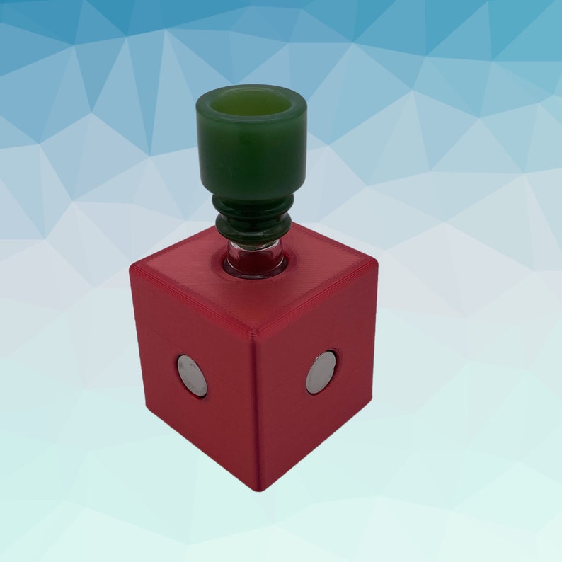 Puede incluir: Un cubo rojo con dos c&iacute;rculos plateados en la parte delantera. Un cuenco de vidrio verde se asienta en la parte superior del cubo.