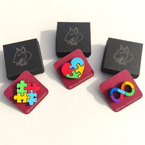May include: An overhead shot of three small, black square boxes and three burgundy-colored square cards. Each card features a colorful puzzle piece design: a square, a heart, and an infinity symbol. The text "@HBA.PORTUGAL" is printed on each card.