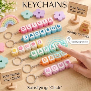 Könnte beinhalten: Anpassbare Clicker-Namensschlüsselanhänger mit bunten quadratischen Blöcken, Buchstaben, Symbolen und Metallringen. Die Schlüsselanhänger zeigen Namen wie OLIVIA, JACKSON, RAFAEL, DALA und MOM sowie dekorative Blumen- und Regenbogenformen.