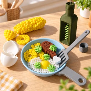 Può includere: Un set da cucina giocattolo con una padella azzurra e una spatola grigia, contenente un uovo al tegamino, un pezzo di carne marrone e guarnizioni verdi. Include una pannocchia gialla, un guscio d'uovo bianco e una bottiglia di olio d'oliva verde scuro con tappo grigio.