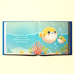 May include: An open book with a blue cover and a colorful illustration of a pufferfish and bubbles. The text on the page reads "Because you love me, Mommy, You help me feel so brave. Like pufferfish who puff with pride, You teach me I'm okay."