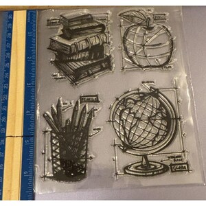 May include: Clear stamp set featuring school-themed designs. Includes illustrations of books, an apple, pencils, and a globe. The stamps are in a sketch style, perfect for crafting and scrapbooking projects.