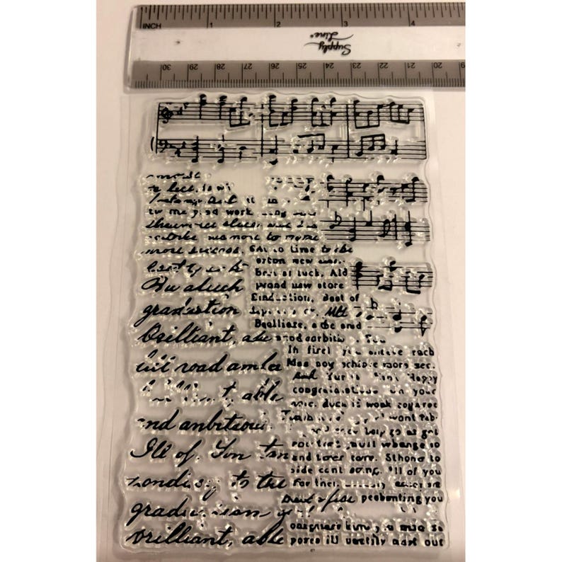 May include: Clear acrylic stamp with musical notes and handwritten script. The stamp includes phrases like "graduation" and "brilliant." A ruler in inches is at the top. Ideal for scrapbooking and card making.