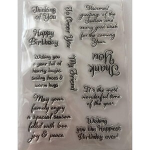May include: A clear sheet of photopolymer stamps featuring various black script phrases including Thinking of You, Happy Birthday, To Cheer You, My Friend, Thank you, and several holiday and seasonal greetings for card making and paper crafts.