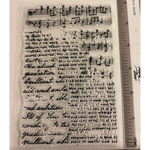 May include: Clear, rectangular stamp with musical notes and handwritten script. The script includes words like "graduation" and "brilliant." A ruler with inch measurements is visible on the right side of the stamp.