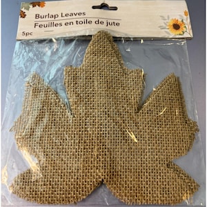 May include: Five burlap leaves in a clear plastic package. The leaves are shaped like maple leaves and are made of a coarse, woven fabric. The package has a label that reads "Burlap Leaves" and "Feuilles en toile de jute".