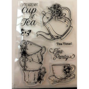 May include: Clear stamp set featuring tea-themed illustrations. Includes a teapot, stacked teacups, a teacup with a saucer, a butterfly, and phrases like "You are my cup of tea" and "Tea Party". Perfect for crafting and scrapbooking.