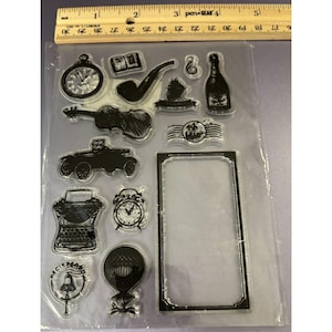 May include: Clear stamp set featuring vintage-themed illustrations. Includes a pocket watch, book, pipe, hat, violin, car, typewriter, alarm clock, and more. The stamps are arranged on a clear sheet with a ruler at the top.