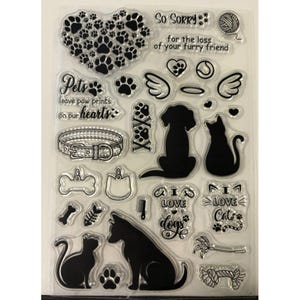 May include: A clear silicone stamp sheet featuring various pet-themed designs including silhouettes of dogs and cats, paw prints, a collar, bones, a fish skeleton, a ball of yarn, angel wings, and text such as So Sorry for the loss of your furry friend.