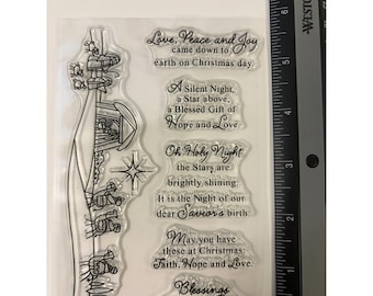 May include: A clear photopolymer stamp sheet featuring a nativity scene illustration and Christmas-themed text. A Westcott ruler is visible on the right side, showing the sheet measures approximately 7 inches in length along the vertical edge.