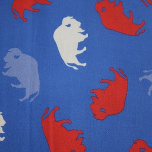 Op de afbeelding: Blauwe stof met een herhalend patroon van rode en witte buffelsilhouetten.