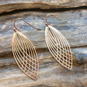 Puede incluir: Un par de pendientes de oro rosa con un diseño de hoja geométrico. Los pendientes están hechos de finos hilos de metal que crean un patrón delicado e intrincado.