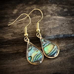 Könnte beinhalten: Ein Paar goldene Tropfenohrringe mit irisierenden Abalone-Muscheleinlagen.