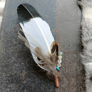 Może przedstawiać: Biało-czarne pióro z brązowymi oznaczeniami, ozdobione kolorowymi koralikami i literami "KIM" w srebrze.