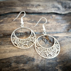 Op de afbeelding: Zilveren oorbellen met een cirkelvormig ontwerp met ingewikkelde swirls en uitsnijdingen. De oorbellen hebben een eenvoudige haaksluiting.