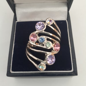 May include: A silver ring with a multi-colored swirl design. The ring is adorned with small, round, colorful gemstones.