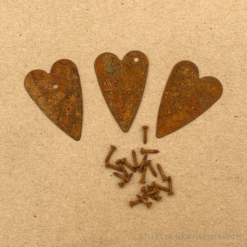 Puede incluir: Tres adornos en forma de coraz&oacute;n de metal oxidado con peque&ntilde;os agujeros en la parte superior y un mont&oacute;n de tornillos oxidados. Los corazones y los tornillos est&aacute;n sobre una superficie marr&oacute;n claro.