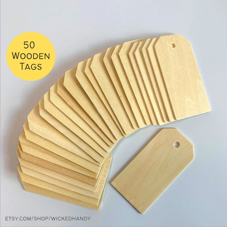 May include: Fifty natural wood tags with rounded corners and a hole punched in the top. The tags are arranged in a fan shape with one tag laying flat on the table.
