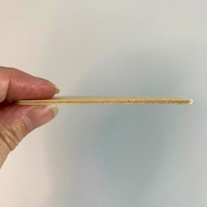 May include: A close-up of a thin, light brown piece of plywood. The plywood is held horizontally in a hand, showing the layers of wood.