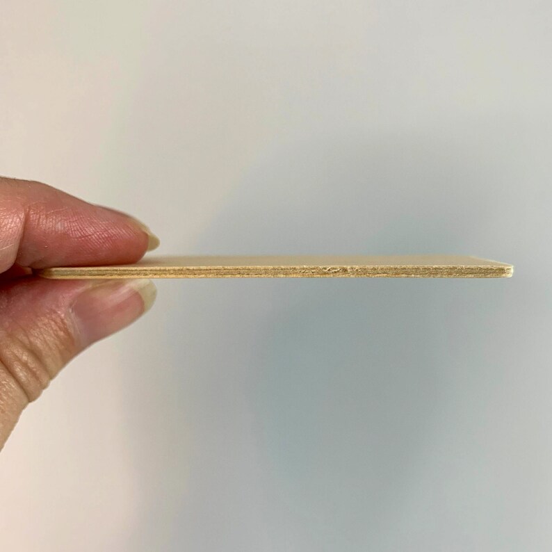 May include: A close-up of a thin, light brown piece of plywood. The plywood is held horizontally in a hand, showing the layers of wood.
