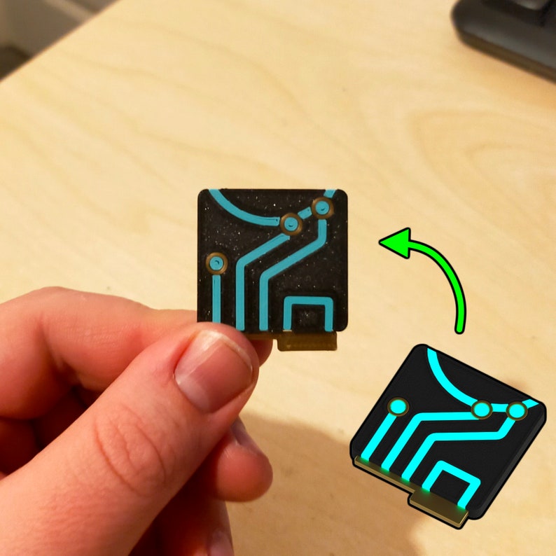 Puede incluir: Una peque&ntilde;a placa de circuito negro con un dise&ntilde;o azul y dorado. La placa tiene una superficie texturizada y es aproximadamente del tama&ntilde;o de una moneda de 20 c&eacute;ntimos de euro.