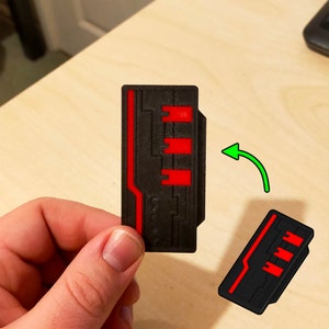 Puede incluir: Una tarjeta de llave impresa en 3D de color negro y rojo con un dise&ntilde;o de placa de circuito. La tarjeta de llave se sostiene en una mano y se gira para mostrar ambos lados.