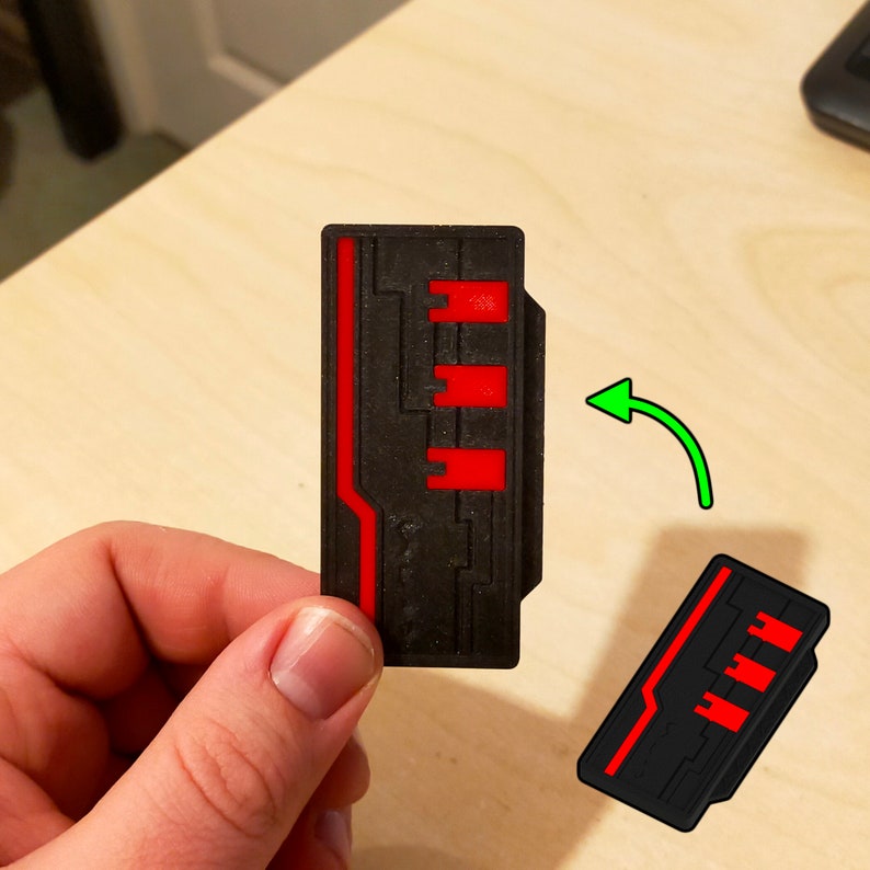 Puede incluir: Una tarjeta de llave impresa en 3D de color negro y rojo con un dise&ntilde;o de placa de circuito. La tarjeta de llave se sostiene en una mano y se gira para mostrar ambos lados.