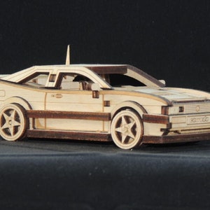 Op de afbeelding: Een houten modelbouwpakket van een witte Volkswagen Golf, met een gedetailleerd interieur en exterieur. Het model is ongemonteerd en wordt geleverd met instructies.