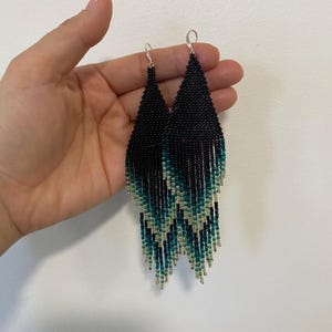 Könnte beinhalten: Ein Paar schwarze und türkisfarbene Perlenohrringe mit Fransen. Die Ohrringe sind lang und hängen herunter.