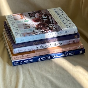 May include: A stack of five hardcover books featuring titles Open Your Eyes by Alexandra Stoddard, Simply Flowers by Barbara Milo Ohrbach, Antiques At Home, Antique Furniture: How to Tell the Real Thing from a Fake, and Antiques Table by Sheila Chefetz.