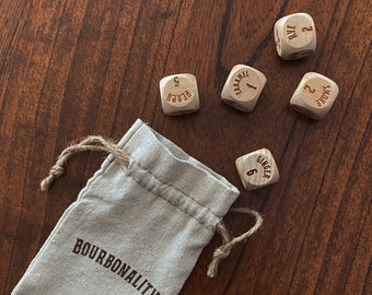 May include: A small, beige drawstring bag with the word "BOURBONALITY" printed on it.  The bag is surrounded by six wooden dice with different words and numbers printed on them. The words on the dice are "Rye", "Caramel", "Spice", "Ginger", and "Peach".