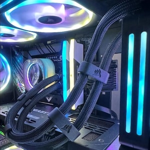 May include: A close-up of a computer's internal components, including a black and white motherboard, a black and blue CPU cooler, and black braided cables with black cable ties. The cables are labeled "GIGABYTE".