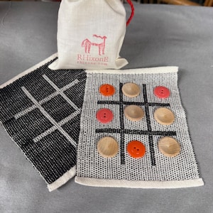 May include: A handmade tic-tac-toe game set with a black and white woven board and wooden game pieces. The set includes a drawstring bag with a red horse logo and the text "RHixonE rhixone.com".