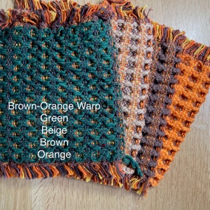 以下が含まれることがあります： 緑、ベージュ、茶色、オレンジの織り生地見本をクローズアップ。生地は、質感のあるワッフル織りのパターン。緑色の見本には「Brown-Orange Warp」の文字が見える。