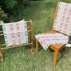 Puede incluir: Dos toallas de cocina tejidas con un patrón de cuadros rosa y verde. Una toalla está doblada y se muestra en un toallero de madera, mientras que la otra está drapeada sobre una silla de madera.
