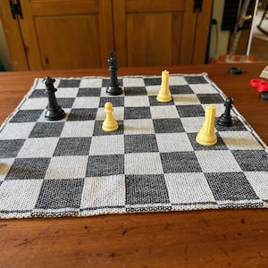 Puede incluir: Un tablero de ajedrez a cuadros blanco y negro con varias piezas de ajedrez en juego. Las piezas de ajedrez son negras y color crema. Hay piezas de damas en la mesa.