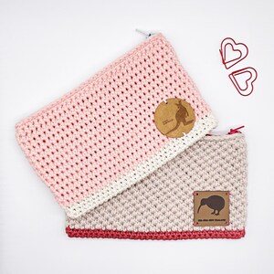 Könnte beinhalten: Zwei gehäkelte Reißverschlusstaschen, eine rosa und weiß mit einem braunen Känguru-Etikett, die andere beige mit rotem Rand und einem braunen Kiwi-Etikett mit der Aufschrift "Kia Ora New Zealand".
