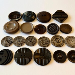 May include: A selection of vintage buttons in shades of brown and black. The buttons are of various sizes, shapes, and designs, including round, square, and textured options. Some have multiple holes, while others have a shank.