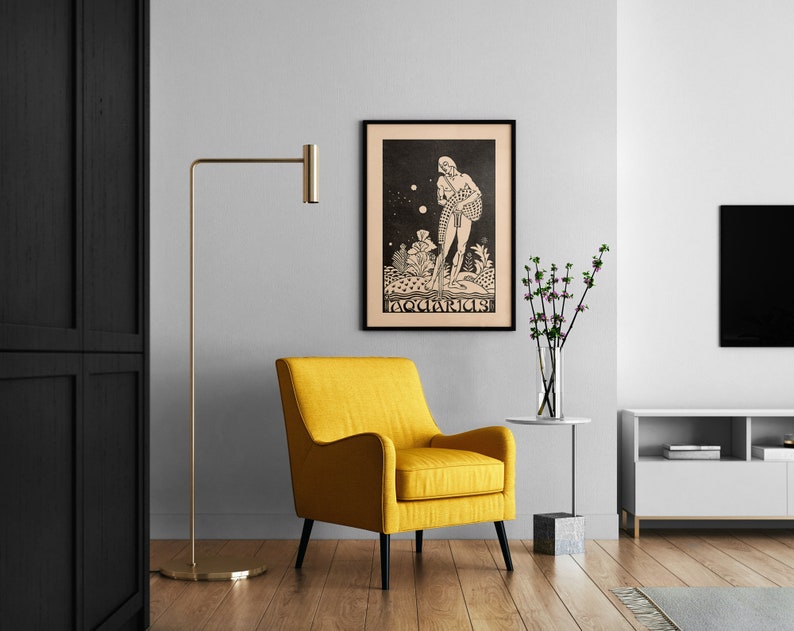 May include: A black and white illustration of the zodiac sign Aquarius, framed in black, hanging on a white wall above a yellow armchair. The illustration depicts a figure pouring water from a jar.