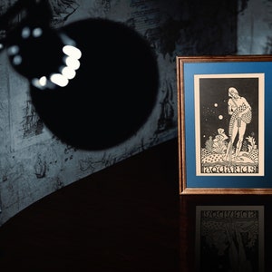 May include: A framed black and white print of an astrological illustration of Aquarius. The image depicts a figure standing in a field of flowers with stars in the background. The text "Aquarius" is printed at the bottom of the image.