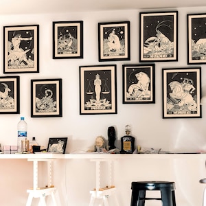 Puede incluir: Una pared blanca con 12 impresiones enmarcadas en negro de signos del zod&iacute;aco. Los signos est&aacute;n en orden de izquierda a derecha: Capricornio, Acuario, Piscis, Aries, Tauro, G&eacute;minis, C&aacute;ncer, Leo, Virgo, Libra, Escorpio, Sagitario. Las impresiones son todas en blanco y negro y tienen un estilo vintage.