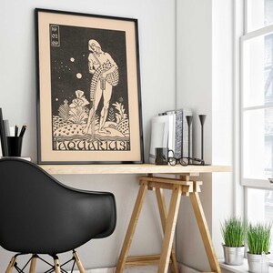 May include: Black and white illustration of a person standing on a small island with the text "Aquarius" below. The image is framed in black and hanging on a white wall above a wooden desk.