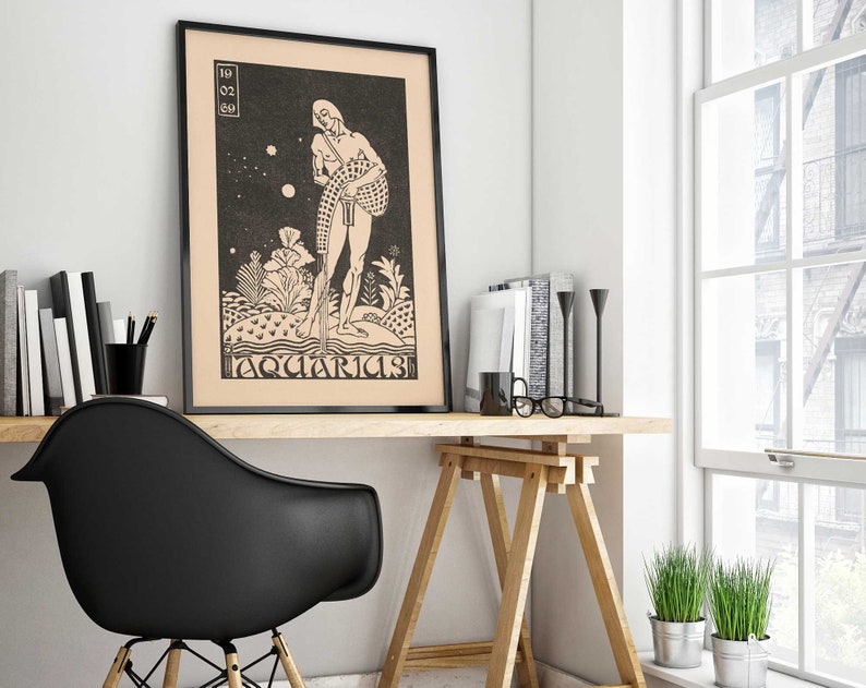 May include: Black and white illustration of a person standing on a small island with the text "Aquarius" below. The image is framed in black and hanging on a white wall above a wooden desk.