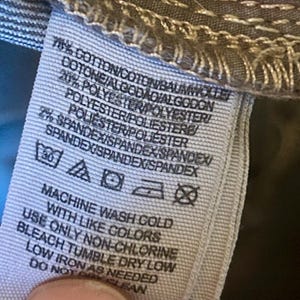 May include: A close-up of a clothing tag with text indicating the fabric composition: 78% cotton, 20% polyester, and 2% spandex. Washing instructions include machine wash cold with like colors, non-chlorine bleach, tumble dry low, and low iron.
