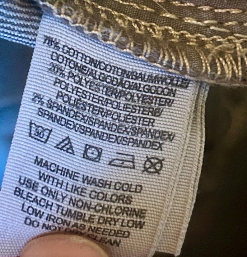 May include: A close-up of a clothing tag with text indicating the fabric composition: 78% cotton, 20% polyester, and 2% spandex. Washing instructions include machine wash cold with like colors, non-chlorine bleach, tumble dry low, and low iron.