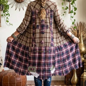 May include: A long, open-front jacket constructed from multiple panels of brown and burgundy plaid flannel fabric. The garment features raw, frayed edges, visible stitching, and several rectangular fabric patches sewn onto the back panel.
