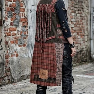 May include: A long, sleeveless vest featuring a patchwork design of dark olive fabric and red plaid panels. The back includes long, hanging fabric fringe, a small rectangular leather-like patch, and distressed detailing throughout the garment.